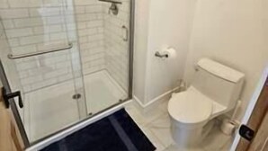 Une salle de bain avec une douche à parois de verre, des toilettes et un petit tapis.