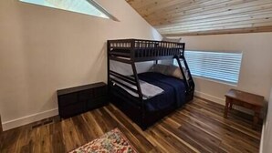 Une pièce avec un lit superposé, une petite table, une fenêtre avec des stores et un plafond en bois.