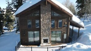 Une cabane en rondins avec une cheminée en pierre, de grandes fenêtres et un toit recouvert de neige.
