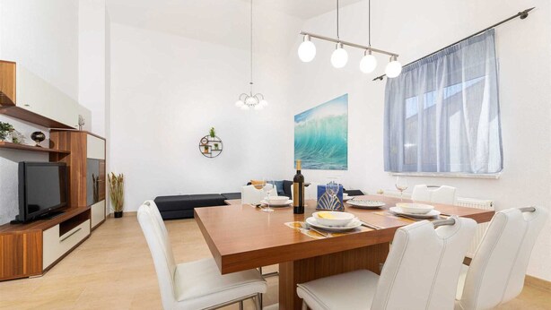 Un espace repas moderne avec une table en bois, des chaises blanches et un tableau représentant une vague accroché au mur.