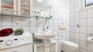 Casa de banho moderna com máquina de lavar, lavatório e sanita.