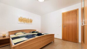 Quarto com cama de madeira, mesa de cabeceira, uma obra de arte na parede e porta de madeira.