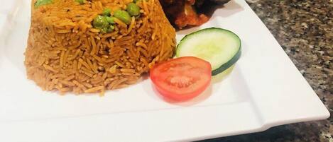 A plate of rice with peas, a slice of tomato, and a cucumber on a granite countertop.