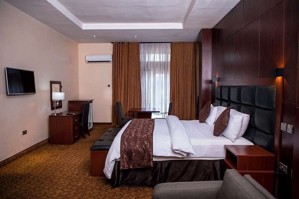 A hotel room with a large bed, a desk, a television, and a window with curtains.