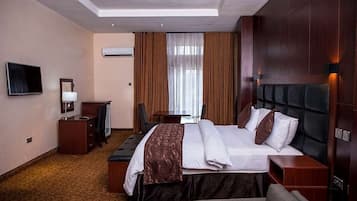 A hotel room with a large bed, a desk, a television, and a window with curtains.