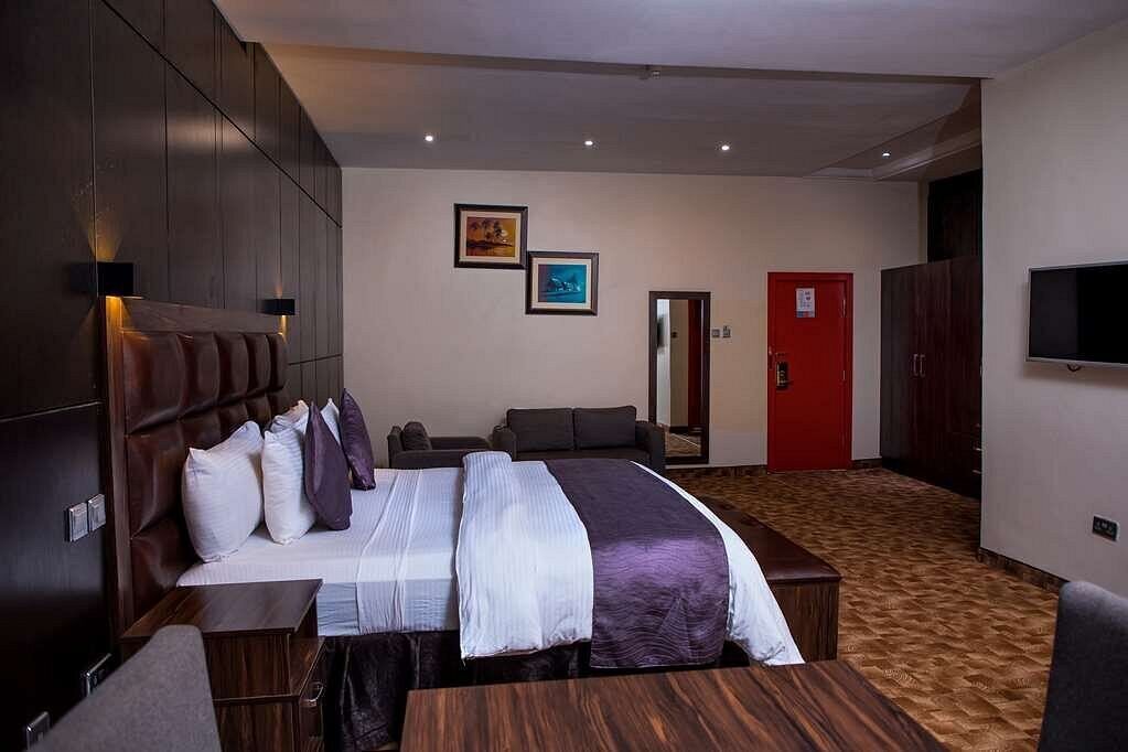 A hotel room with a large bed, a desk, a chair, a TV, and a red door.