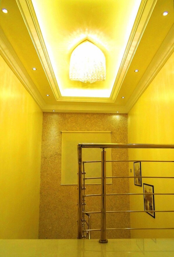 Un hall de hotel con una lámpara de techo luminosa, una barandilla de vidrio y un cuadro en la pared.