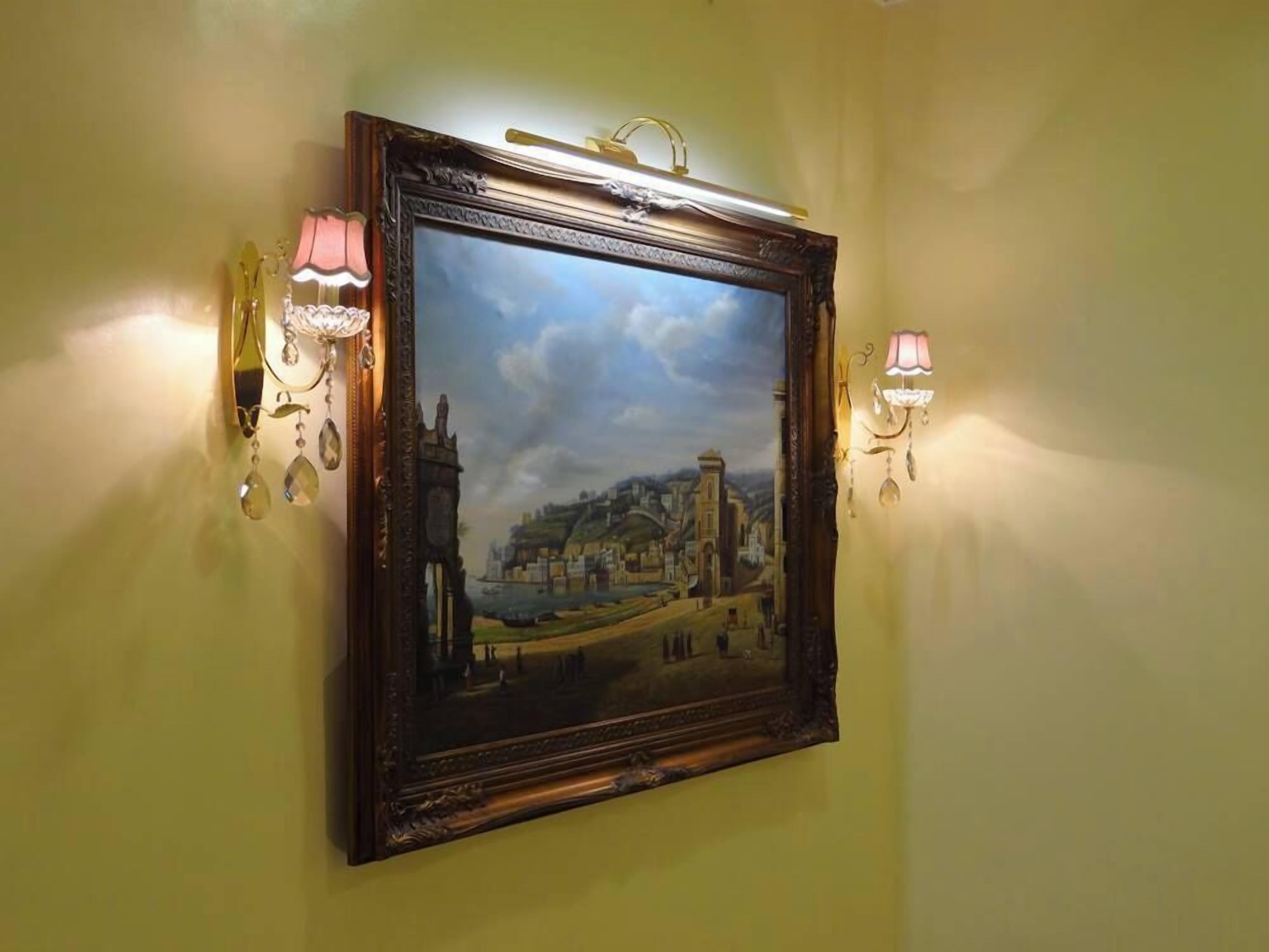 Um quadro emoldurado pendurado numa parede, com duas luminárias de parede.