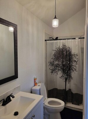 Une salle de bain avec un lavabo blanc, un miroir, des toilettes et un rideau de douche orné d’un motif d’arbre.