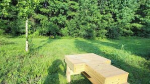 A wooden picnic table in a grassy area with dense trees in the background. - Peaceful and Private Cabin with fun activities for family & friends on 25 Acres (Broaddus)