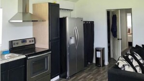 A compact kitchen with a stove, oven, and refrigerator, a ceiling fan, and a door leading to another room. - Peaceful and Private Cabin with fun activities for family & friends on 25 Acres (Broaddus)