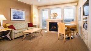 A living room with a sofa, a coffee table, a fireplace, a dining table with chairs, a ceiling fan, and a framed picture on the wall. - 2-bedroom beachfront condo in Seaside with free WiFi, kitchen, and pool. (Seaside)
