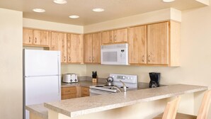 A kitchen with wooden cabinets, a white refrigerator, a microwave, a stove, and a coffee maker. - 2-bedroom beachfront condo in Seaside with free WiFi, kitchen, and pool. (Seaside)