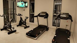 Un gimnasio en casa con cintas de correr, bicicletas estáticas y un televisor montado en la pared.