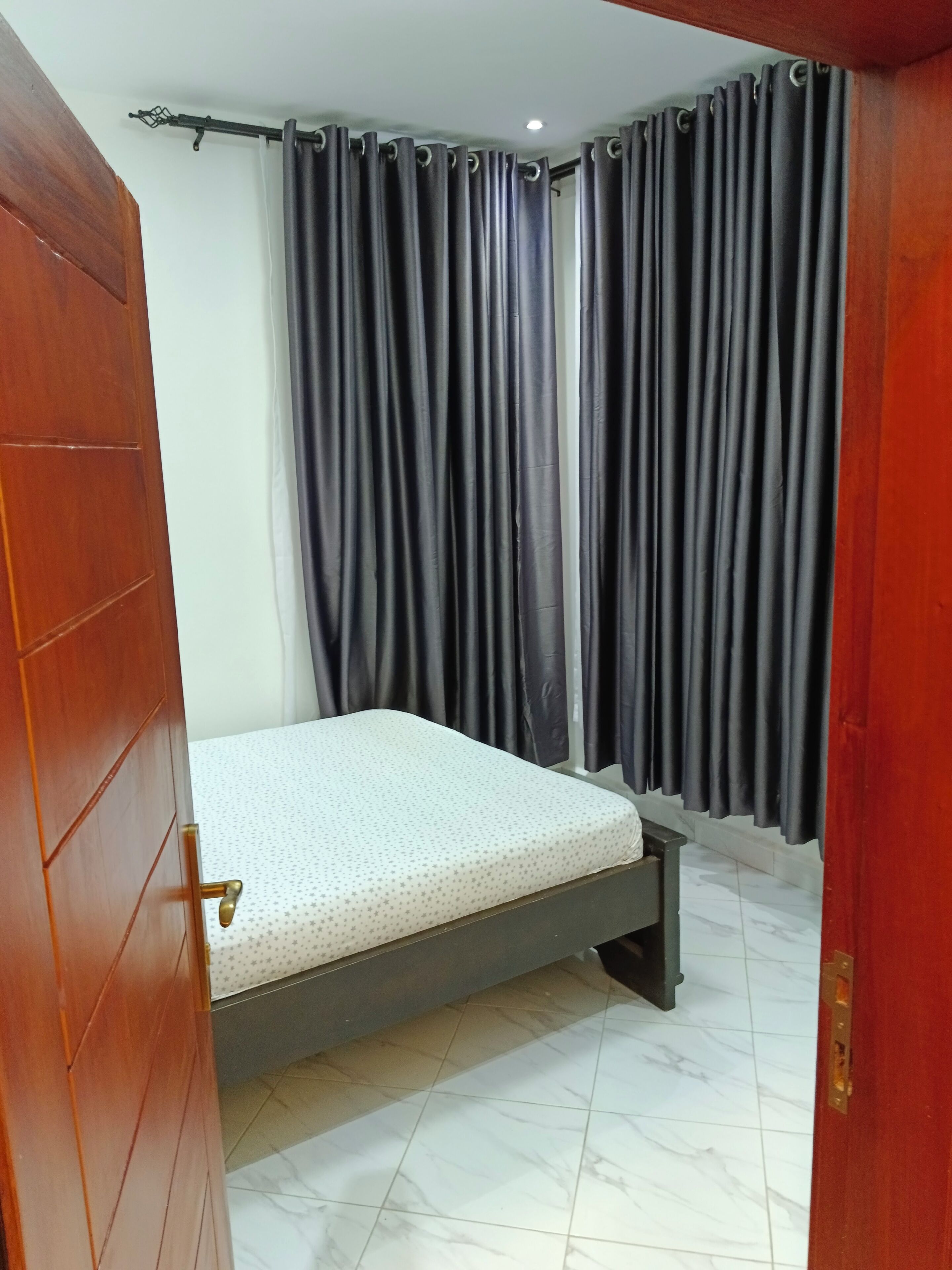A room with a bed, a wooden door, and a curtain.