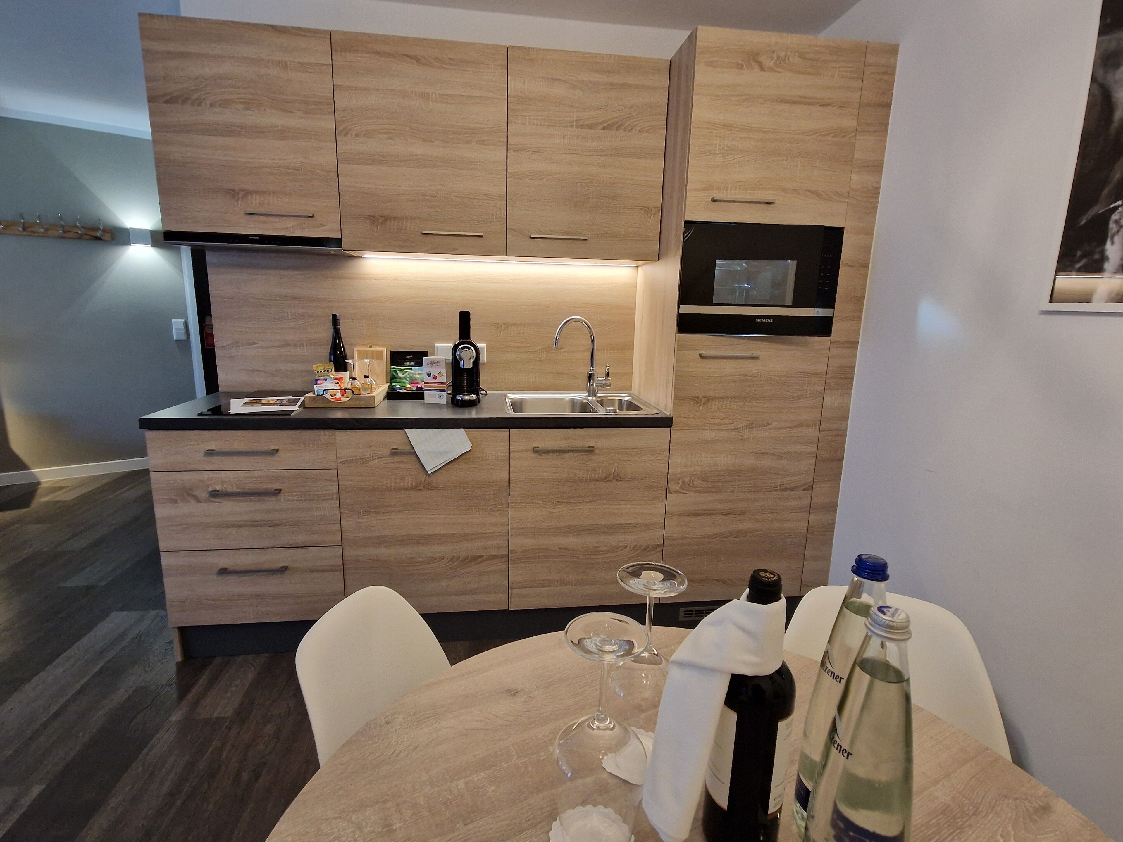 Una cucina moderna con mobili in legno, un forno a microonde integrato e un'area pranzo con tavolo imbandito per due persone.