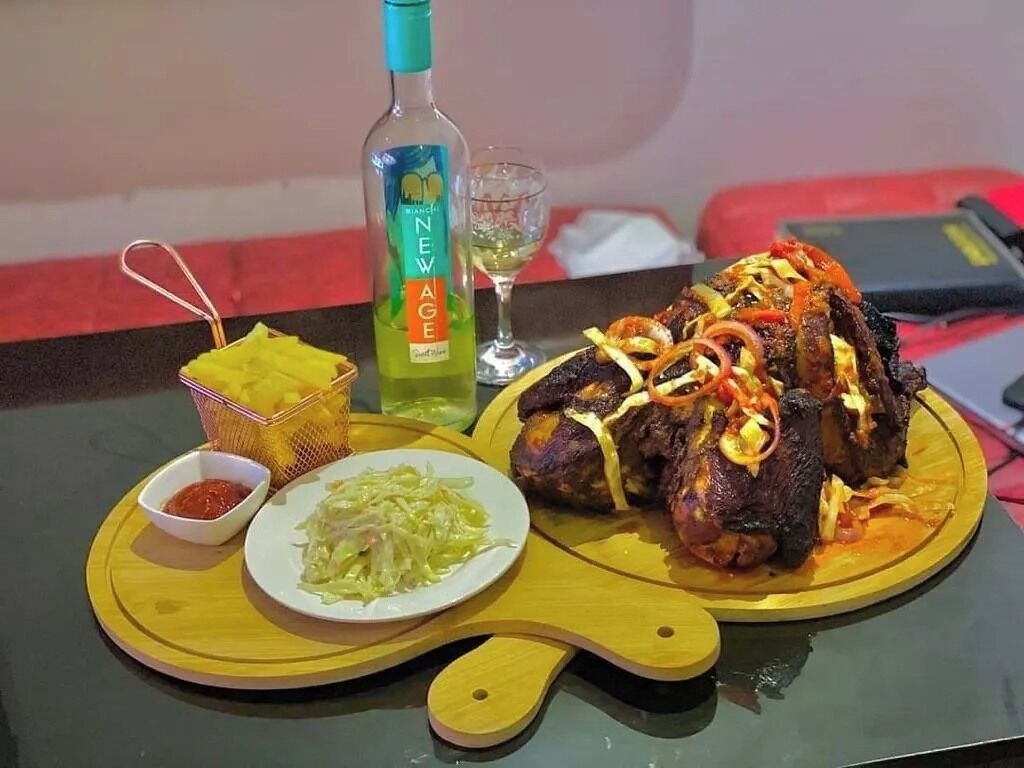 A meal with grilled meat, a bottle of sauce, and a glass of white wine on a table.