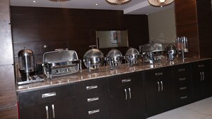 A buffet setup with various food containers and a coffee machine. - BILAD AL-SHAM HOTEL AND SUITES (Kano)