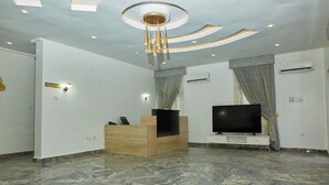 A modern living room with a marble floor, a wooden reception desk, a flat-screen TV, and a ceiling with recessed lighting and a central light fixture. - BILAD AL-SHAM HOTEL AND SUITES (Kano)