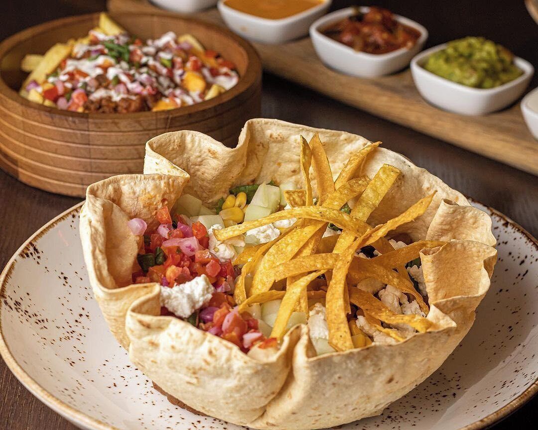 Un bol de nachos garnis de fromage, de tomates et d’oignons, accompagné d’un bol de salsa et de guacamole.