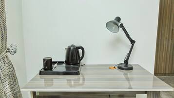 A small workspace with a desk, a kettle, a mug, and a desk lamp.