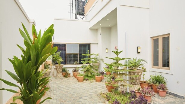 A courtyard with potted plants, a tiled floor, and a building with windows and a water tank. - BILAD AL-SHAM HOTEL AND SUITES (Kano)