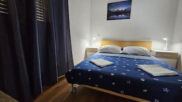 Una cama bien hecha con una colcha azul, dos almohadas blancas y una mesita de noche con una lámpara.