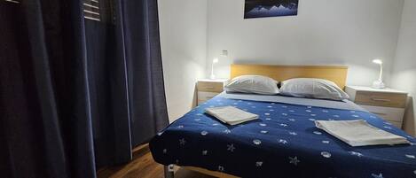 Un lit bien fait, recouvert d’une couvre-lit bleue, avec deux oreillers blancs et une table de chevet sur laquelle se trouve une lampe.