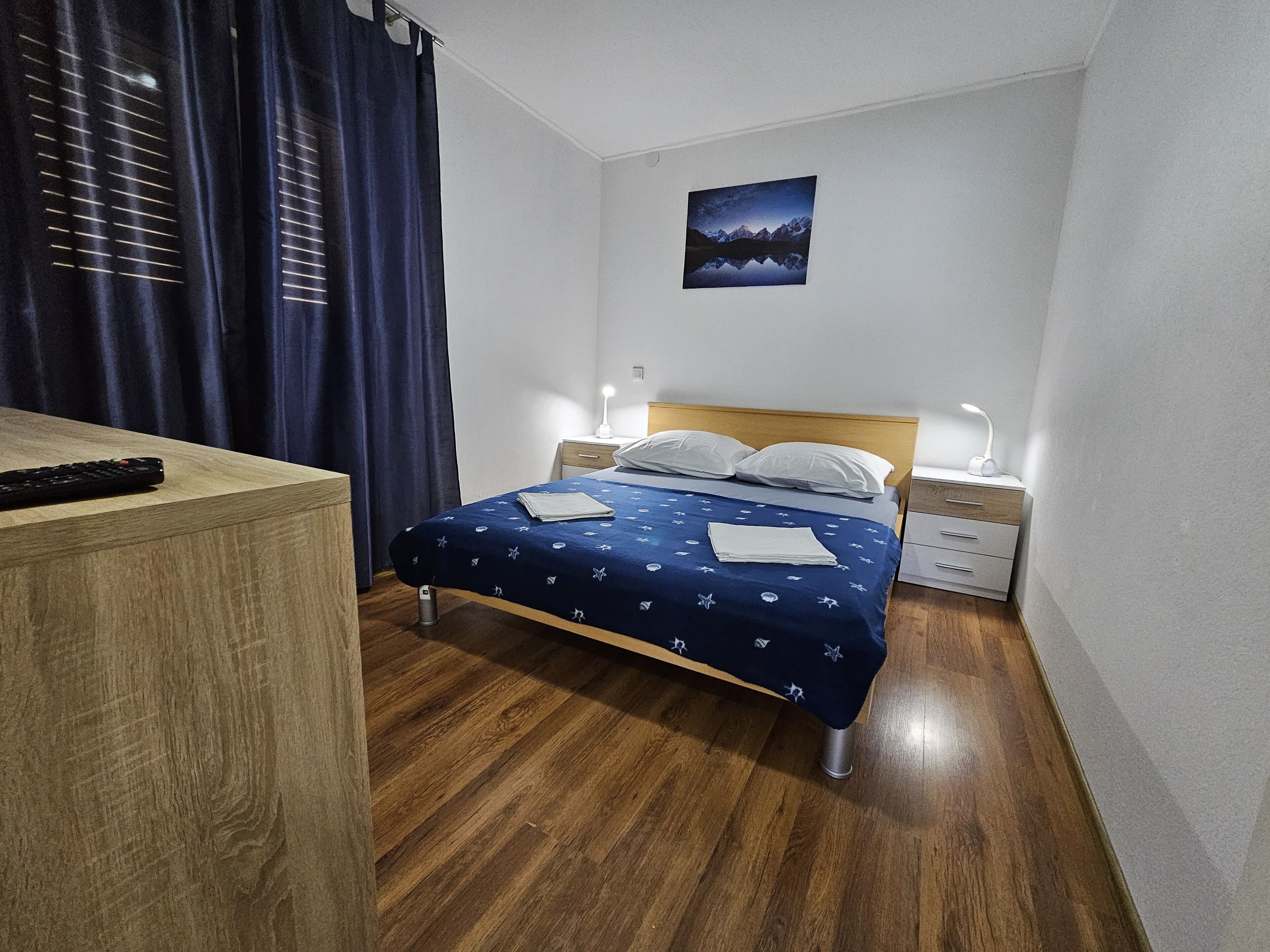 A bedroom with a bed, bedside tables, a nightstand, a remote control, and a painting on the wall.