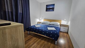 A bedroom with a bed, bedside tables, a nightstand, a remote control, and a painting on the wall.