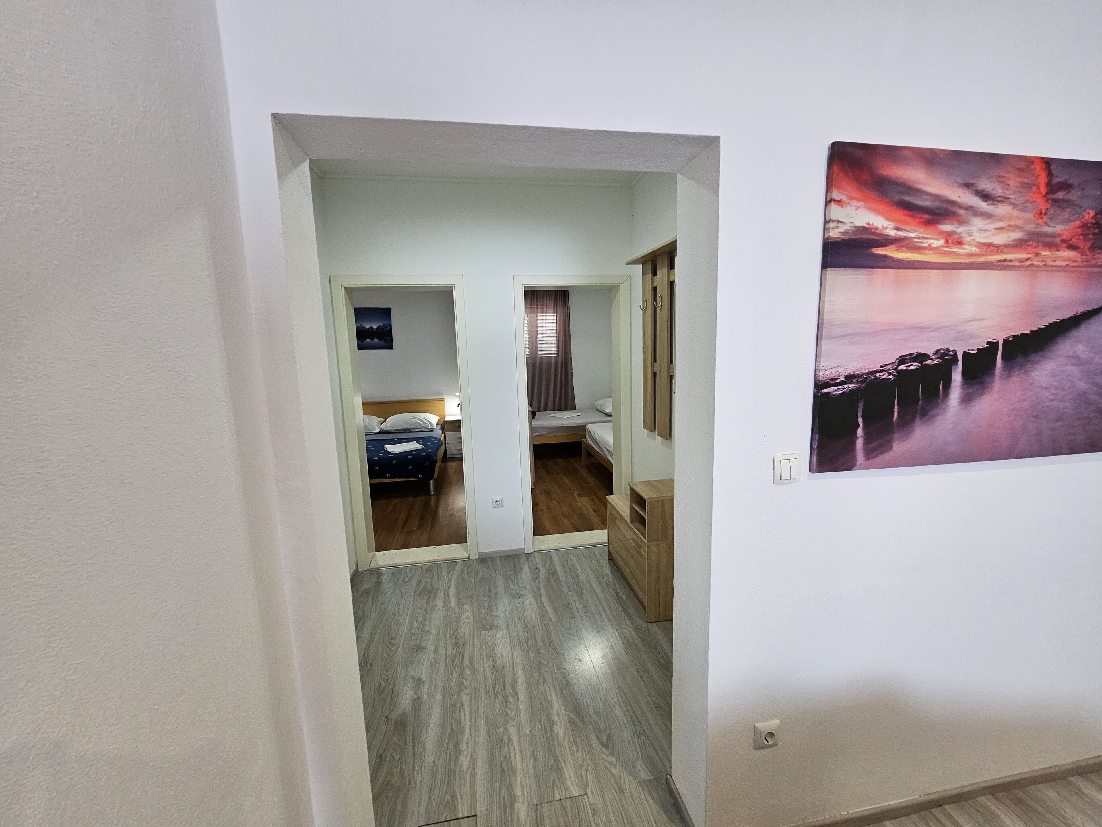 A hallway with a bed, a desk, and a painting on the wall.