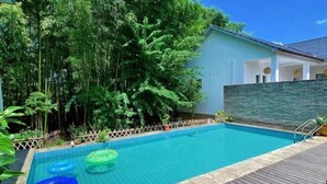 A swimming pool with clear blue water, surrounded by lush greenery and a wooden deck. - Ting San Rice Fields & Yard (Xuancheng)