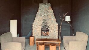 A stone fireplace with a table and two chairs in front, a tall white vase, and a floor lamp. - Ting San Rice Fields & Yard (Xuancheng)