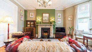 A traditional living room with a fireplace, leather sofas, a chandelier, and framed artwork on the walls. - The Regency Studio (Cardiff)
