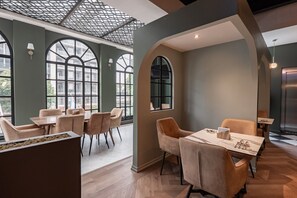 Un comedor moderno con mesas y sillas, ventanas amplias y un techo alto con un diseño geométrico.