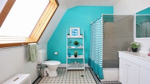 A bathroom with a white toilet, a shelf with plants, a shower curtain, and a tiled floor.