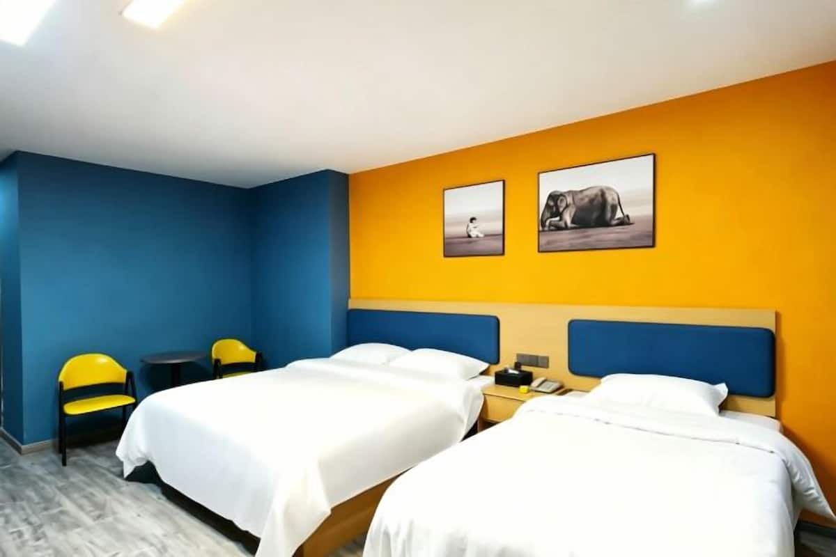 Une chambre d’hôtel avec deux lits, un bureau, des chaises et deux tableaux accrochés au mur.