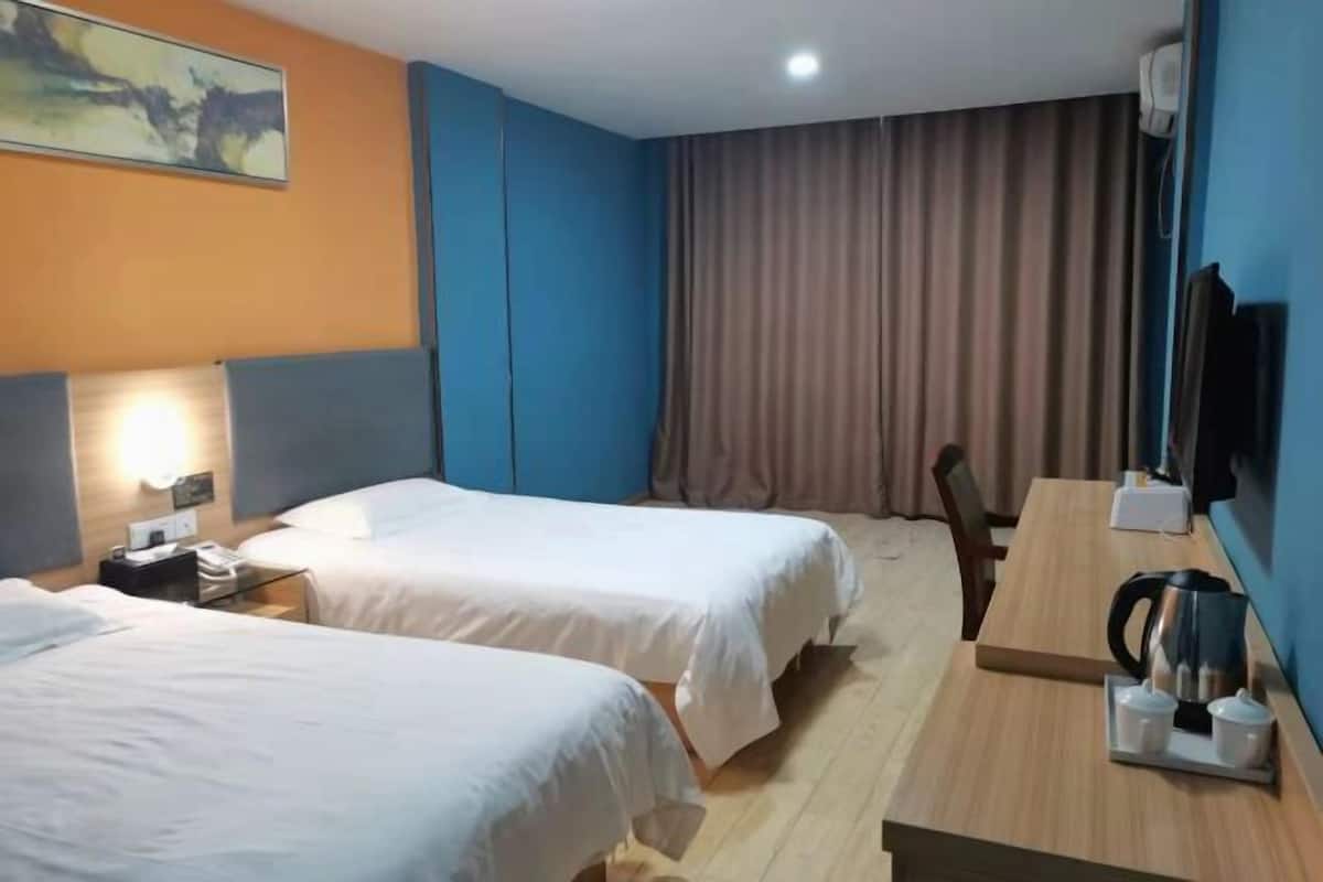 Une chambre d’hôtel avec deux lits, un bureau avec une bouilloire, une télévision et un tableau au mur.