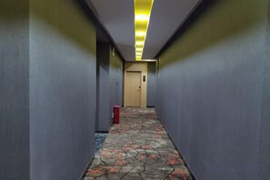Un pasillo con alfombra estampada, un cubo de basura rojo y una puerta al final.