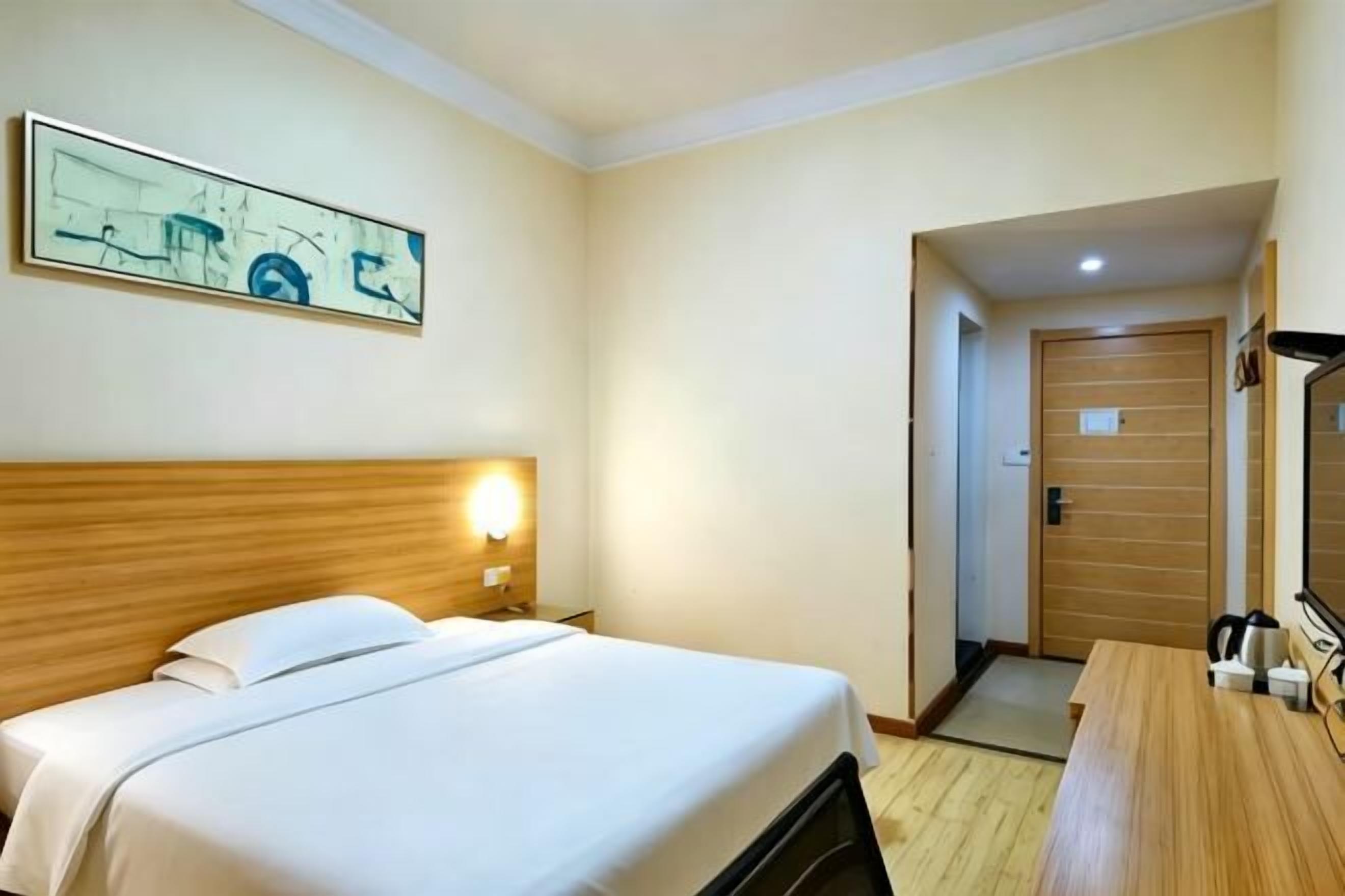 A hotel room with a bed, bedside table, lamp, and a painting on the wall.
