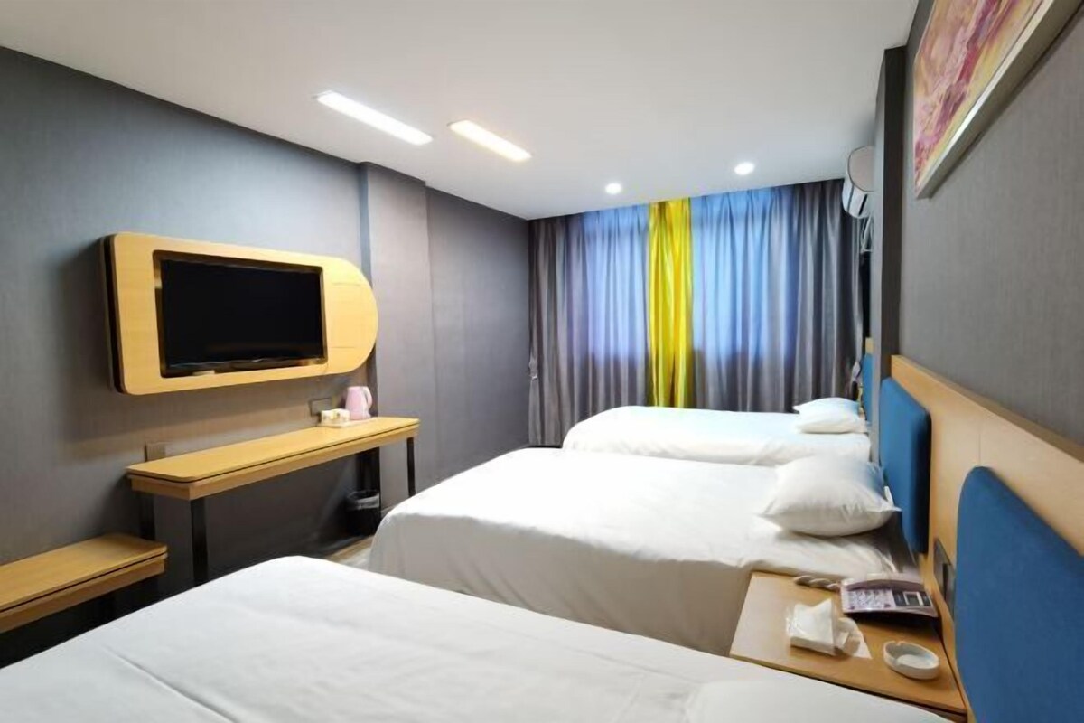 Een hotelkamer met twee bedden, een tv aan de muur, een bureau met stoel en een raam met gordijnen.