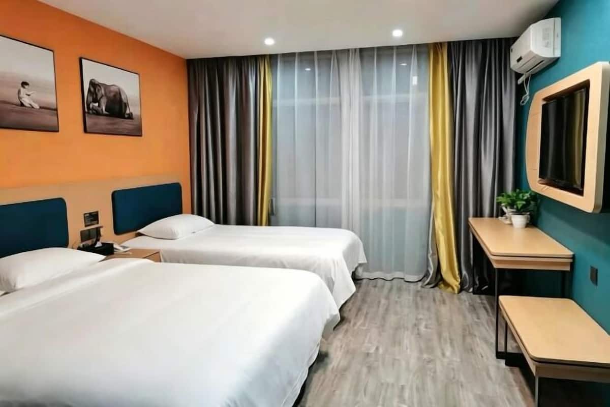 Une chambre d’hôtel avec deux lits, un bureau, une chaise, une télévision et une fenêtre avec des rideaux.