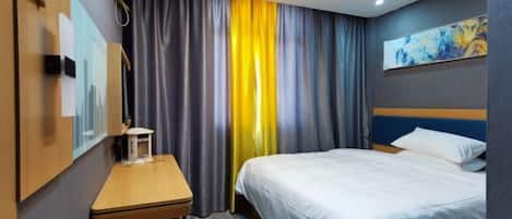 Quarto de hotel com cama, escrivaninha, cadeira, ar condicionado fixado na parede e uma pintura.