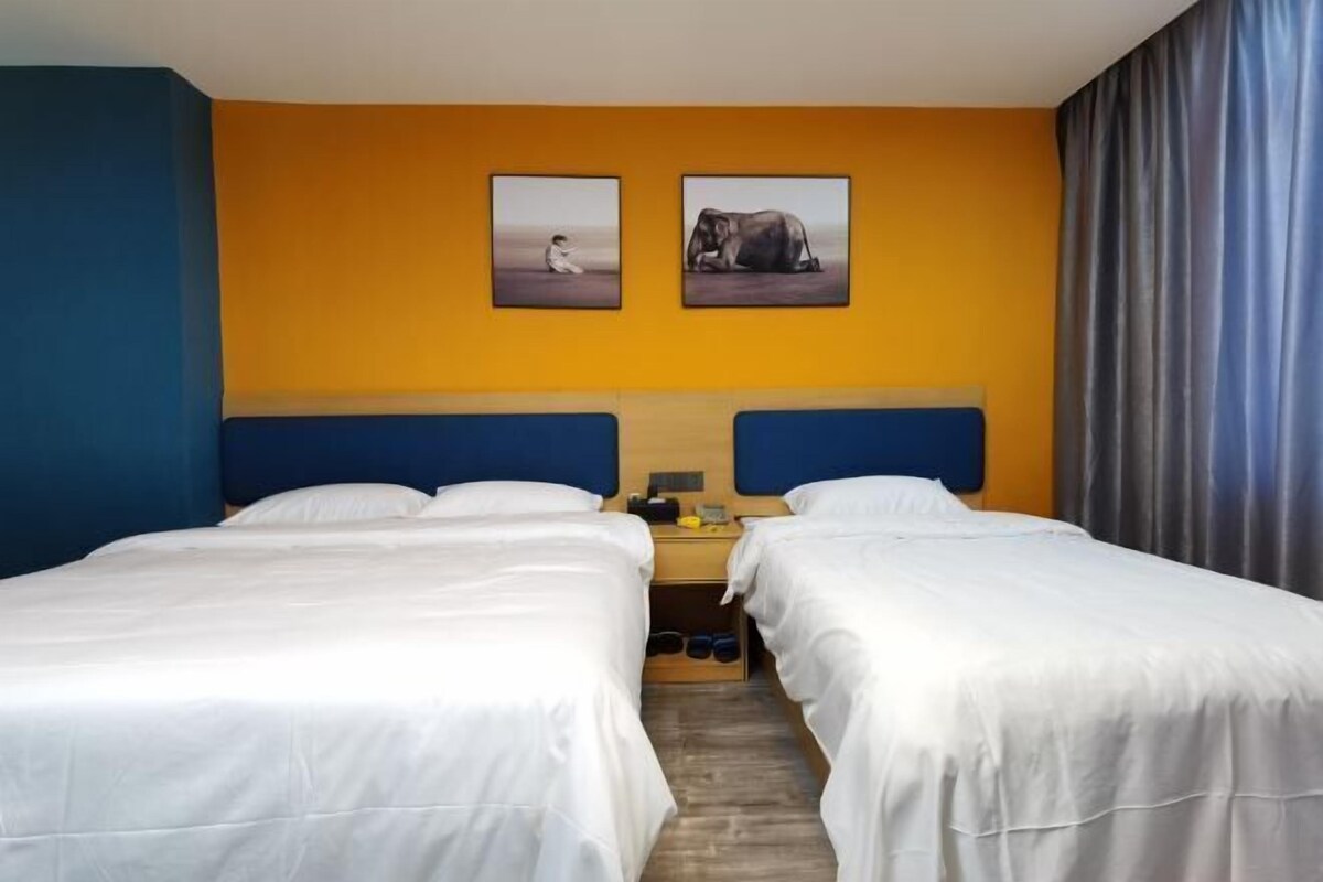 Een hotelkamer met twee bedden, een nachtkastje, een lamp en twee ingelijste foto’s aan de muur.