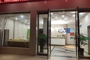 Entrada de hotel con puertas de vidrio, una recepción y zona de baños a la vista.