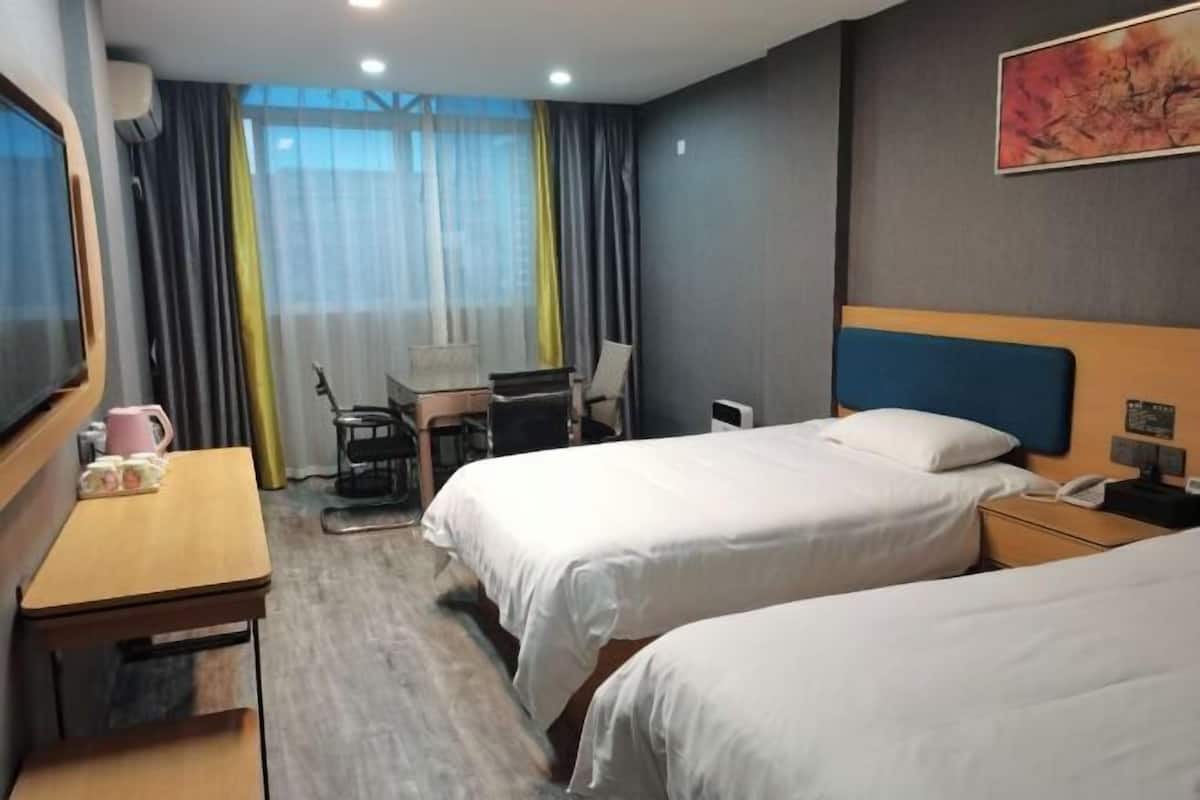 Une chambre d’hôtel avec deux lits, un bureau avec une chaise, une télévision et une fenêtre avec des rideaux.