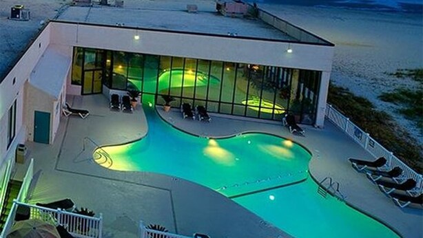 A modern building with a large pool area, outdoor seating, and a view of the beach.