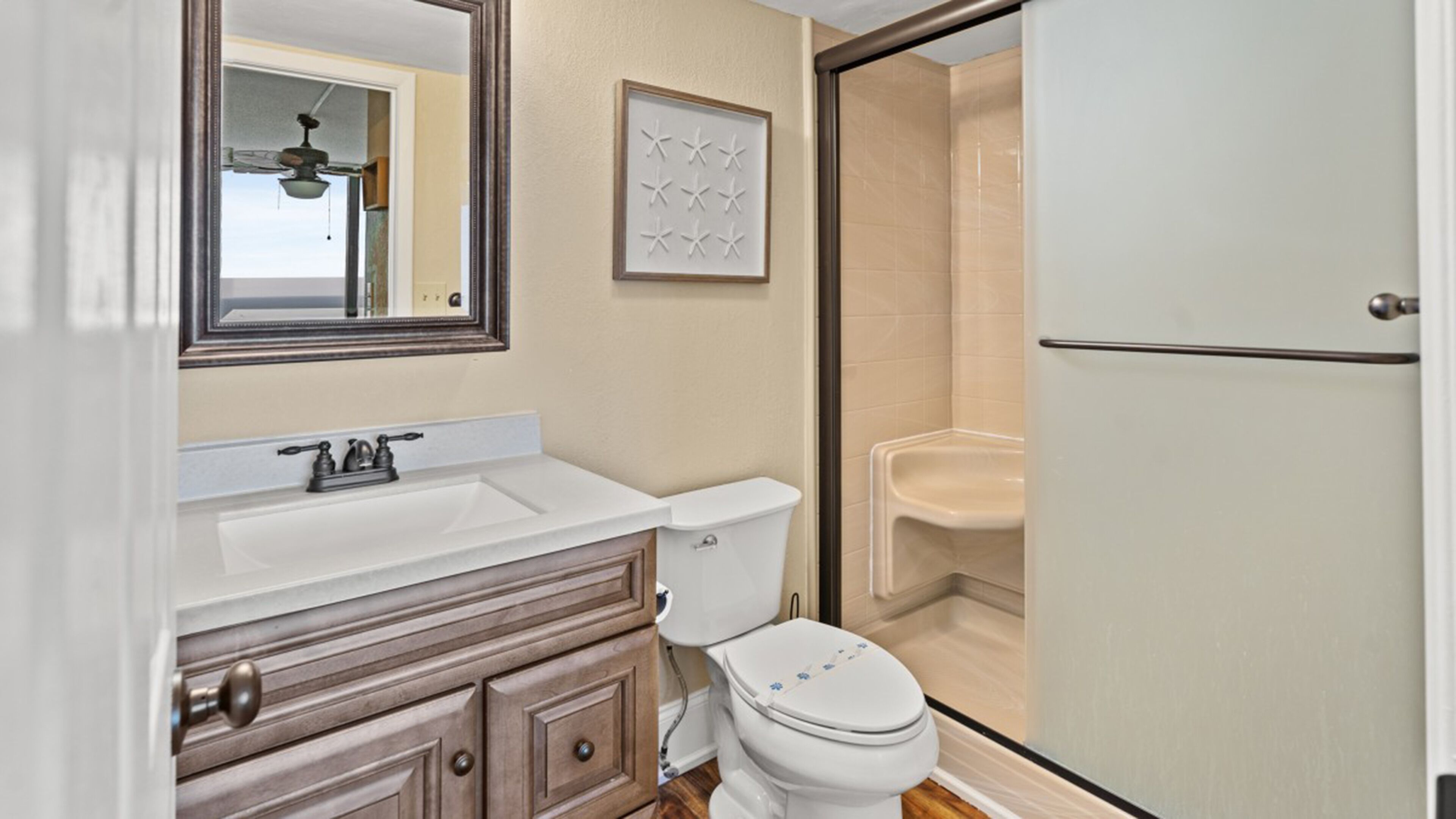 A bathroom with a white sink, wooden vanity, a toilet, and a shower area.