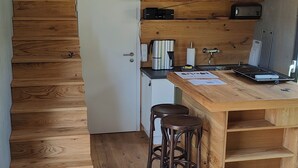 Una cucina compatta con pavimento in legno, un piccolo frigorifero, una macchina per il caffè e un tavolo in legno con sgabelli.