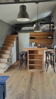 A modern kitchen with a central island, wooden staircase, and bar stools.